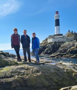 three-people-on-rock-beside-lighthouse