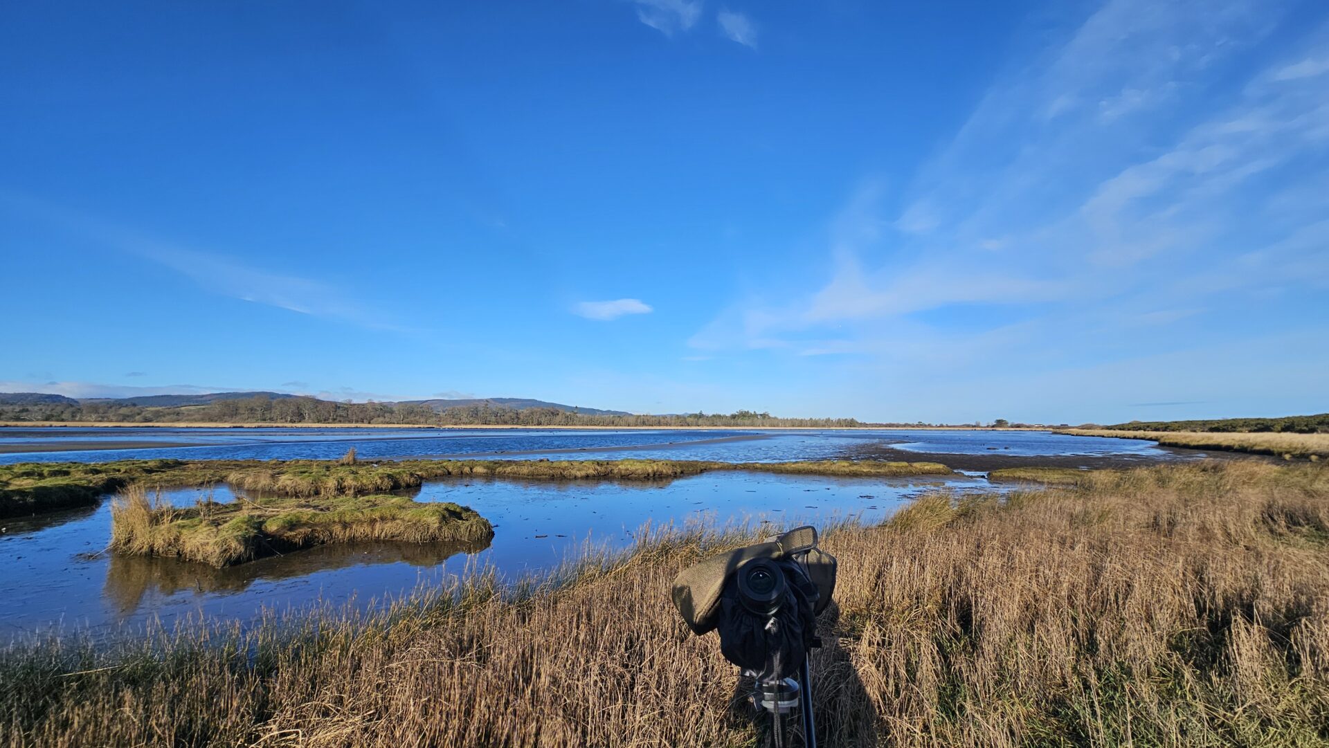 spotting-scope-looking-out-over-wetland-with-blue-sky-and-mountainous-background